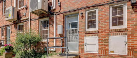 A red brick building with multiple windows, a door, and air conditioning units.