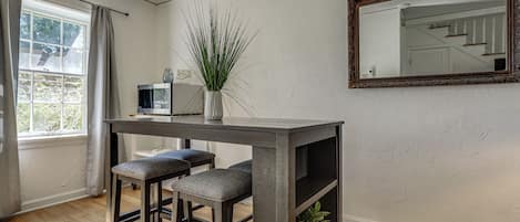 A room with a wooden table, two barstools, a potted plant, a television, and a mirror on the wall.