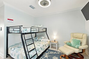 A bunk bed with a warning sign, a small bedside table with a lamp, a chair, and a patterned rug. - Gulf View Home w/ Private Pool, Firepit, and Wraparound Porch | Sleeps 9 (Pensacola Beach)