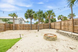 A backyard with a stone fire pit, a wooden fence, and palm trees. - Gulf View Home w/ Private Pool, Firepit, and Wraparound Porch | Sleeps 9 (Pensacola Beach)