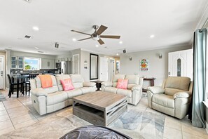 A spacious living room with a ceiling fan, a dining area with a table and chairs, and a kitchen in the background. - Gulf View Home w/ Private Pool, Firepit, and Wraparound Porch | Sleeps 9 (Pensacola Beach)