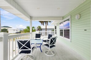A covered outdoor area with a table and chairs, a white railing, and a view of the surrounding area. - Gulf View Home w/ Private Pool, Firepit, and Wraparound Porch | Sleeps 9 (Pensacola Beach)