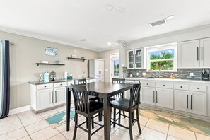 A modern kitchen with white cabinets, a dining table with chairs, and a window with a view of greenery. - Gulf View Home w/ Private Pool, Firepit, and Wraparound Porch | Sleeps 9 (Pensacola Beach)