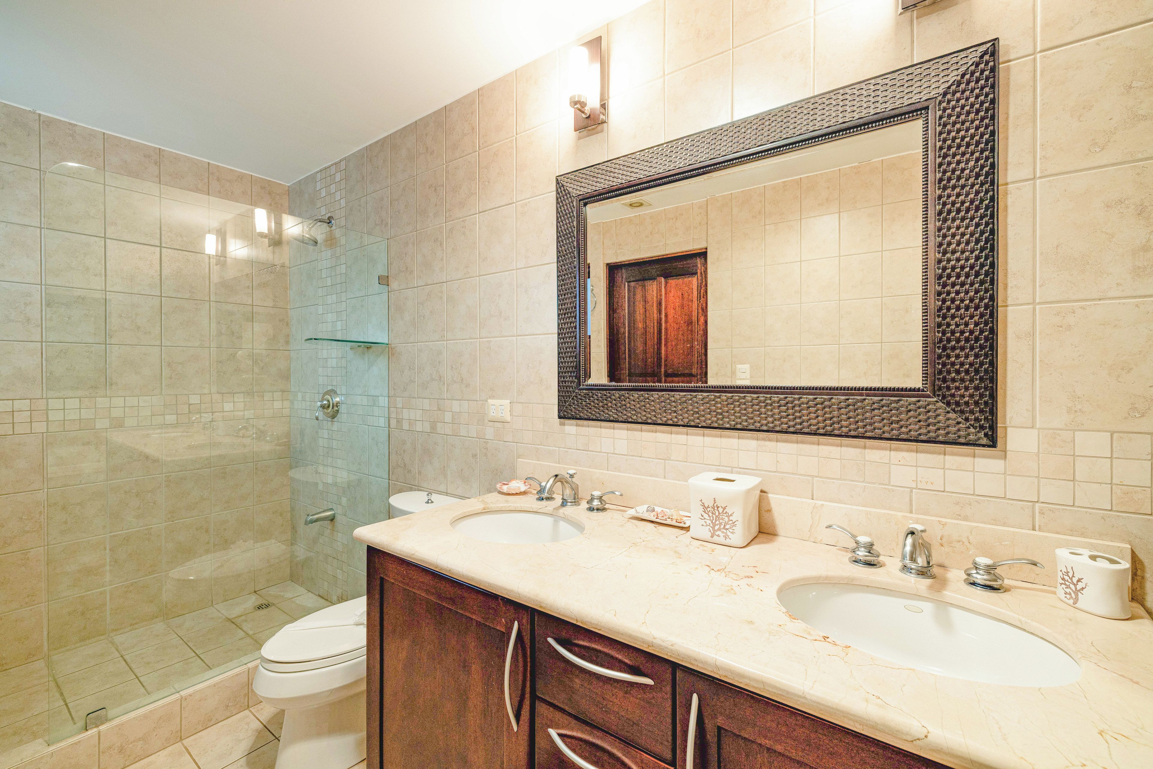 A bathroom with a large mirror, two sinks, a shower, and a toilet.