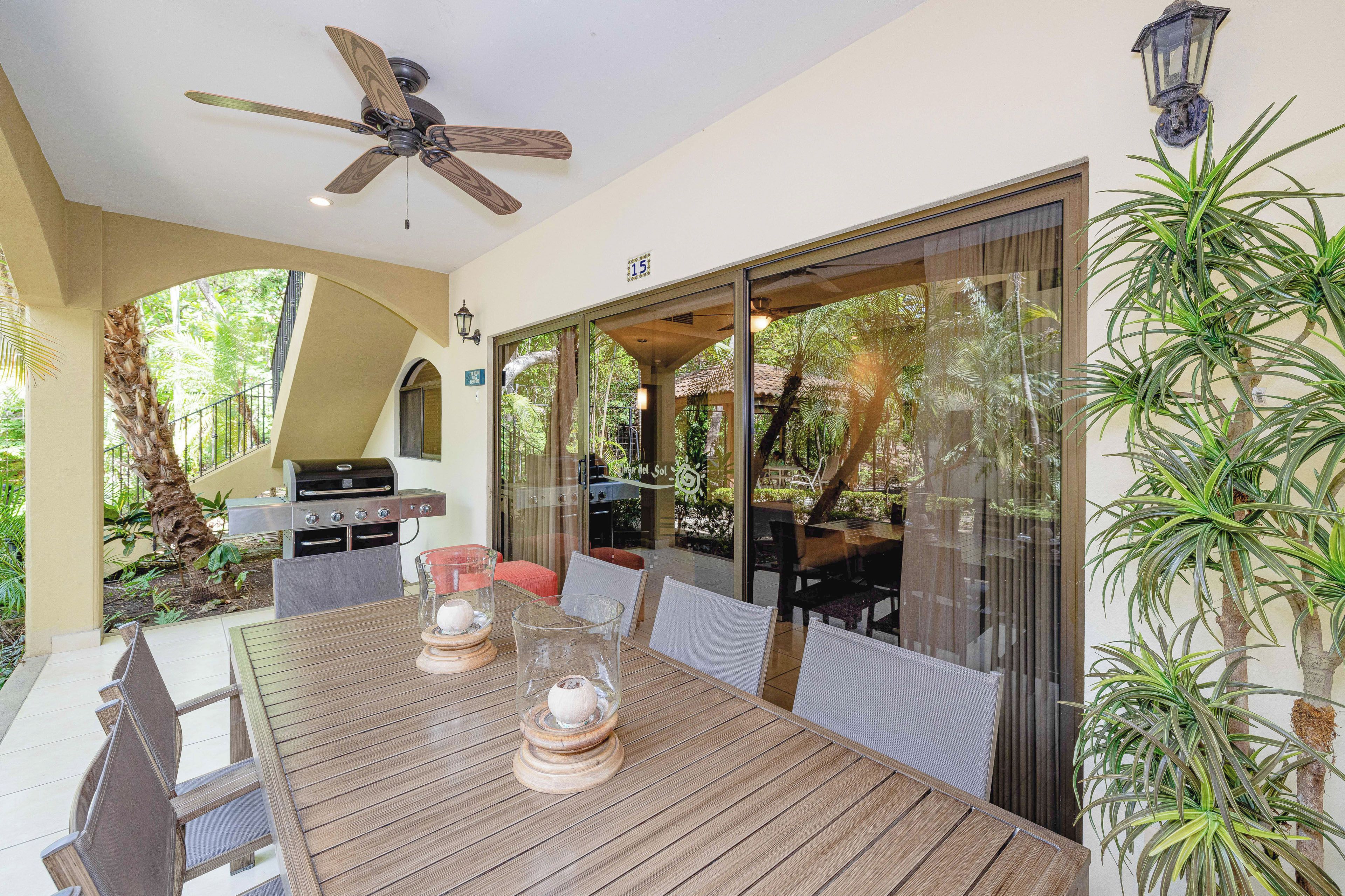 An outdoor dining area with a wooden table, chairs, a ceiling fan, and a grill.