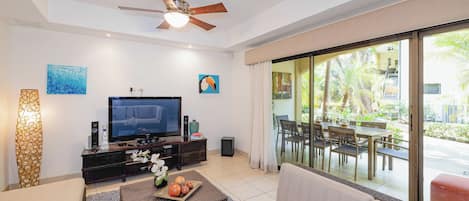 A living room with a flat-screen TV, a ceiling fan, and a dining area with a glass door leading to an outdoor space.