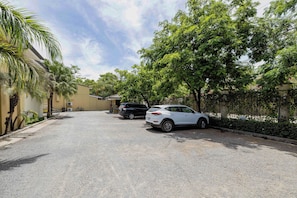 A residential street with two parked cars, a building with a flat roof, and lush greenery.
