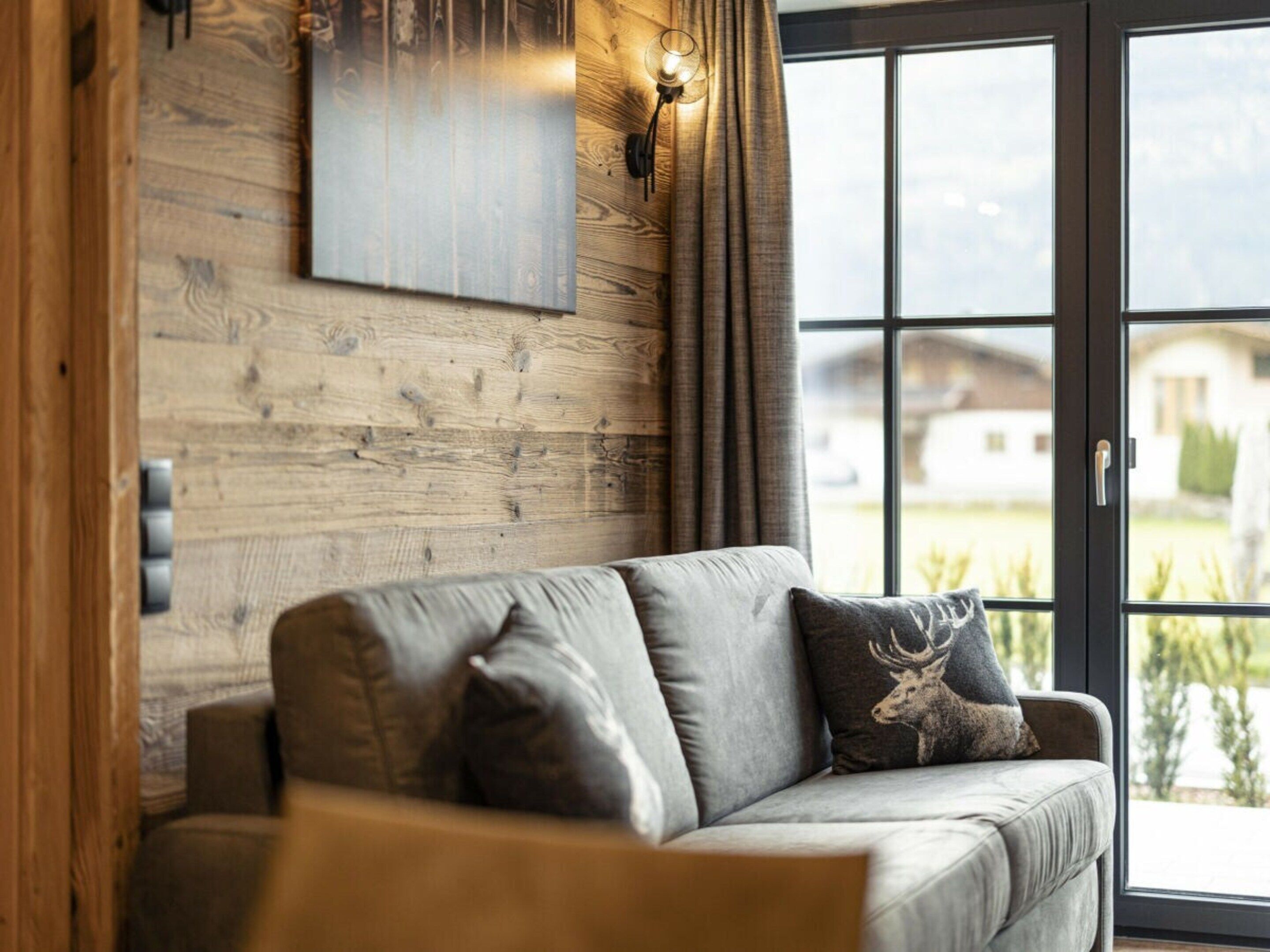 Een moderne woonkamer met een bank, een wandlamp en een groot raam met uitzicht op de omgeving.