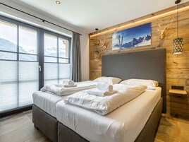 Quarto moderno com uma cama grande, vista para as montanhas, painéis de madeira e um chifre de veado fixado na parede.