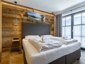 A modern bedroom with a large bed, wooden panel walls, a mountain view, and decorative deer antlers. - Superior Holiday Apartment # 1C With Sauna (Uttendorf)