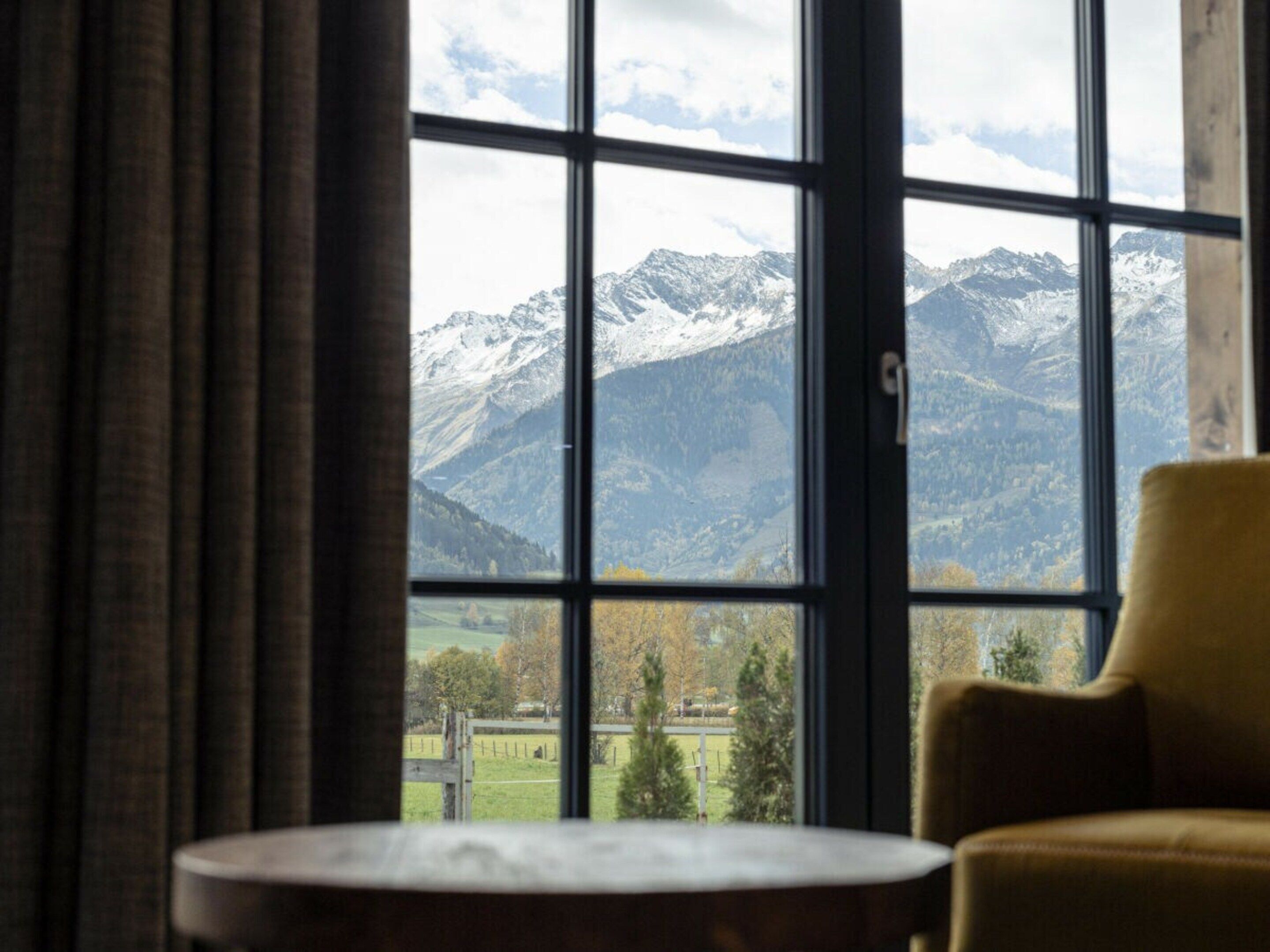 A room with a large window offering a view of snow-capped mountains and a green landscape.