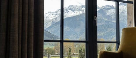 Een kamer met een groot raam, met uitzicht op besneeuwde bergen en een groen landschap.