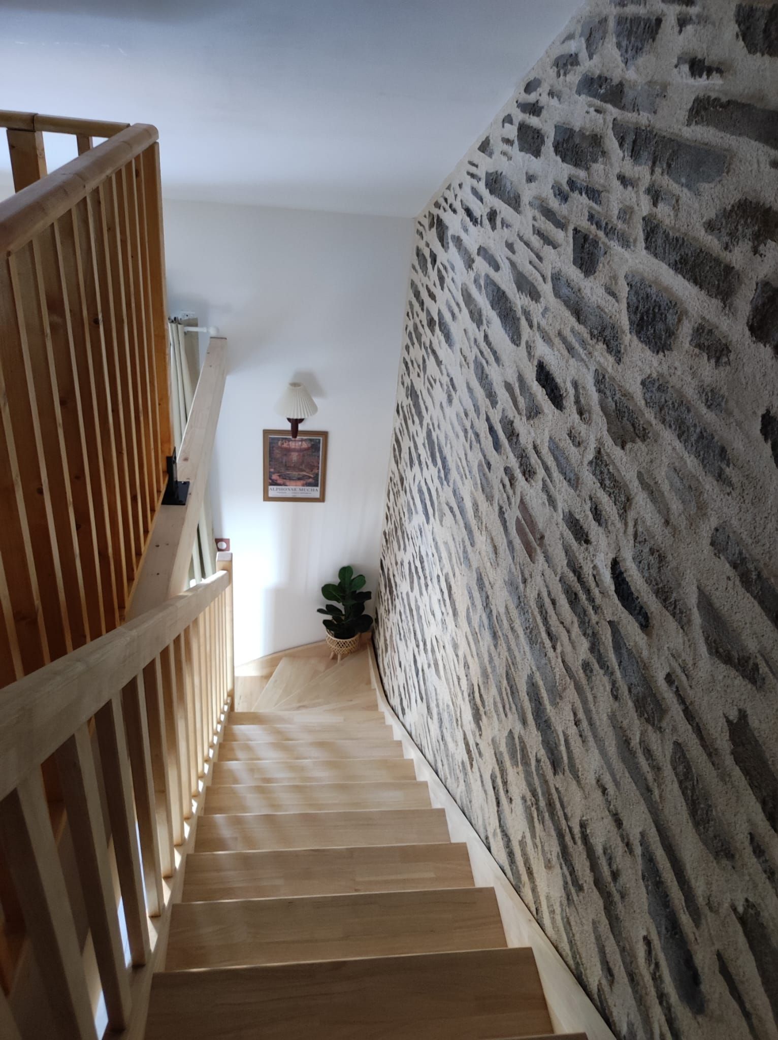 Eine Treppe mit Holzhäuschen führt zu einer Zwischenebene, begleitet von einem Holengeländer auf der einen Seite und einer strukturierten Wand auf der anderen.