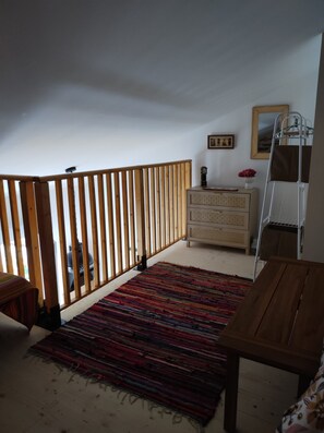 A room with a wooden railing, a dresser, a mirror, and a colorful rug. - Elena's Little House (Cholet)