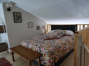 A bedroom with a bed, a wooden bench, a bedside table, and a wall-mounted lamp. - Elena's Little House (Cholet)