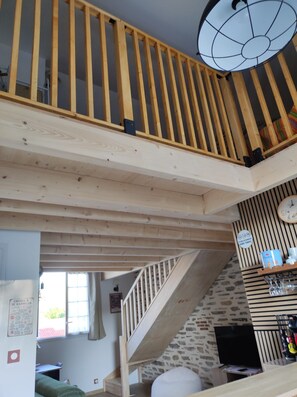 A multi-level wooden interior with a staircase, a ceiling light fixture, and a wall-mounted shelf with items. - Elena's Little House (Cholet)