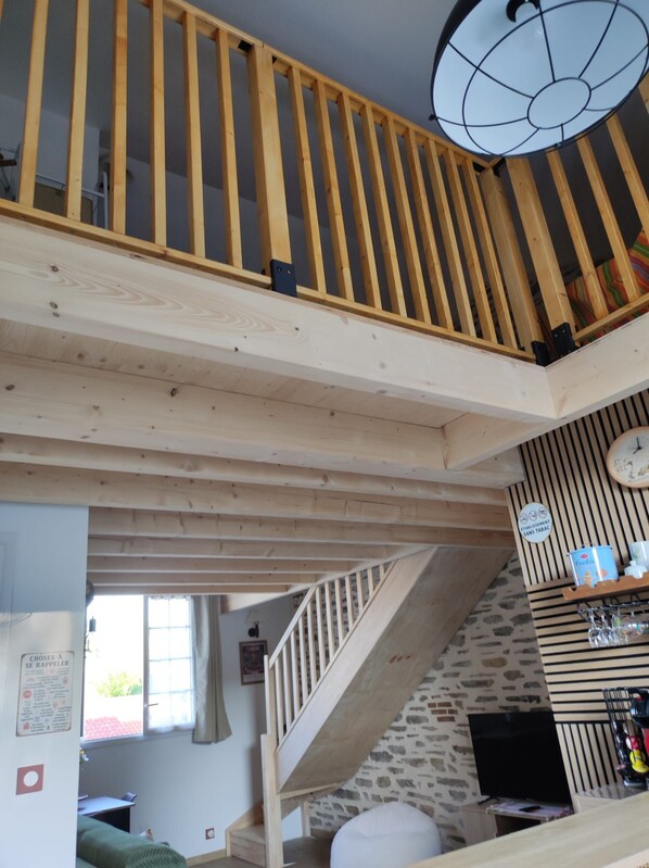A multi-level wooden interior with a staircase, a ceiling light fixture, and a wall-mounted shelf with items.