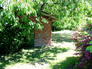 Ein Backsteinhaus mit einer kleinen Tür, umgeben von üppigem Grün und einem Rasenweg.