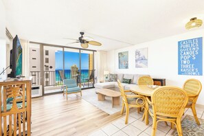A spacious living area with a balcony overlooking the sea, furnished with a sofa, chairs, and a dining table. - Waikiki Banyan 25th-Floor-Ocean View 1BR with Parking (Honolulu)