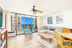A spacious living room with a balcony, a ceiling fan, and a view of the ocean. - Waikiki Banyan 25th-Floor-Ocean View 1BR with Parking (Honolulu)