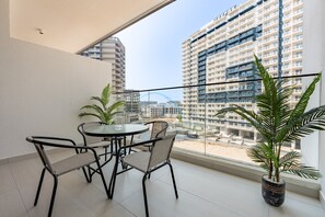Ein Balkon mit Tisch und Stühlen, Blumentöpfen und Blick auf hohe Gebäude.