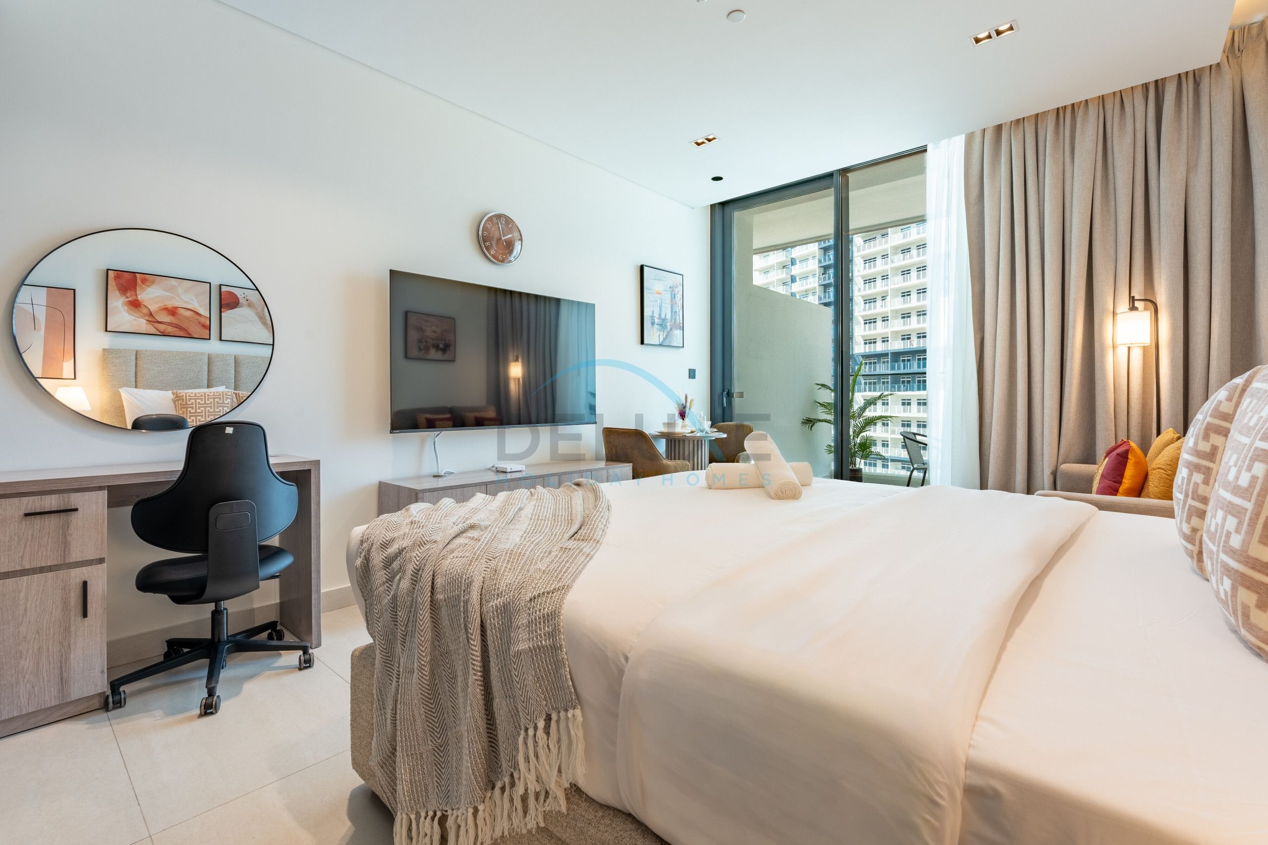 A modern hotel room with a bed, desk, chair, and a large window offering a city view.