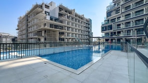 Una piscina con bordo piastrellato e ringhiera metallica, circondata da edifici moderni con balconi.