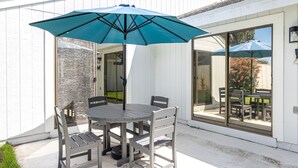 En udendørs terrasse med et rundt bord og fire stole, en blå parasol og en stenvæg.
