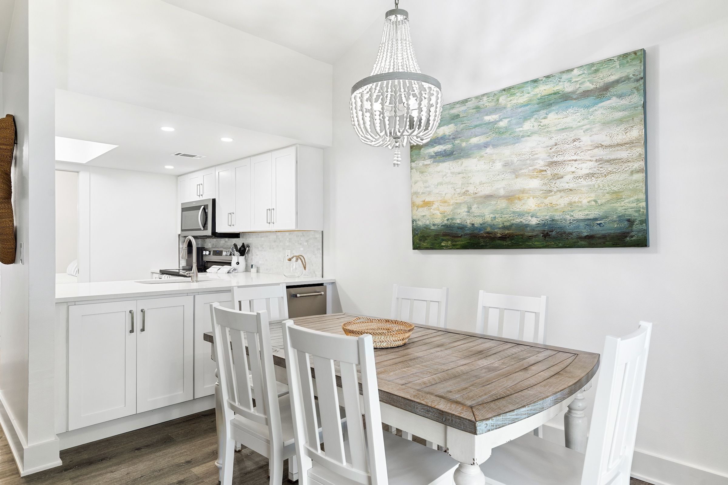 Una cocina moderna con muebles blancos, una mesa de comedor de madera y una lámpara de araña.