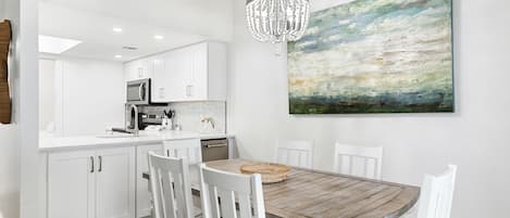 A modern kitchen with white cabinetry, a wooden dining table, and a chandelier.