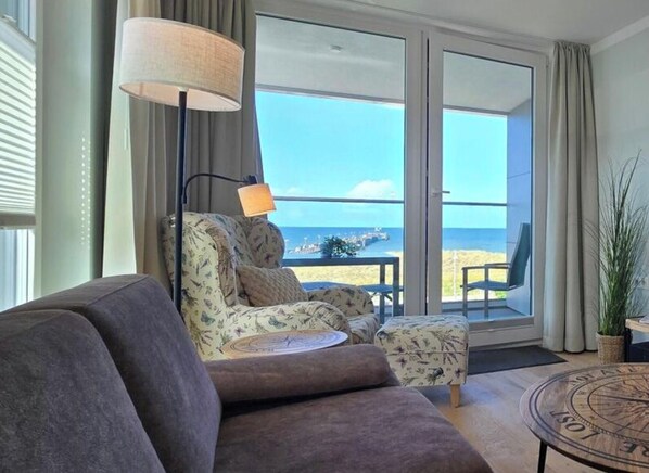A room with a sofa, a chair, a small table, a lamp, and a view of the sea through large windows. - Holiday Apartment i15 - "sea Rush" (Graal Mueritz)