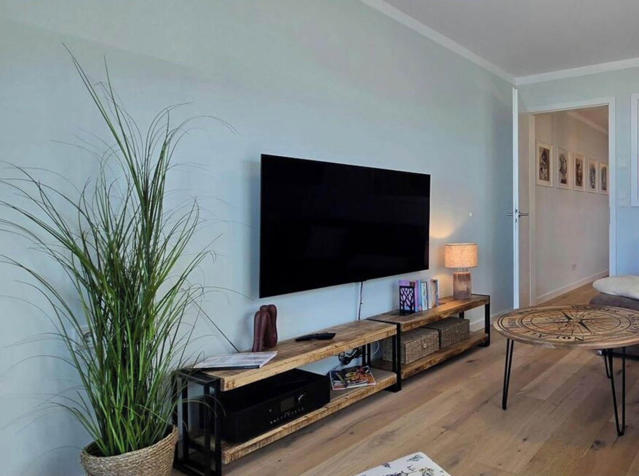 A living room with a flat-screen TV mounted on the wall, a wooden console table with a lamp, and a large potted plant.