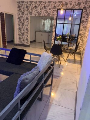 Una habitación con una cama, un comedor con sillas y una mesa, y una cocina al fondo.