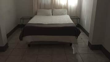 A standard hotel room with a bed, curtains, and a tiled floor.