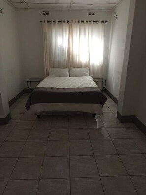 A standard hotel room with a bed, curtains, and a tiled floor.