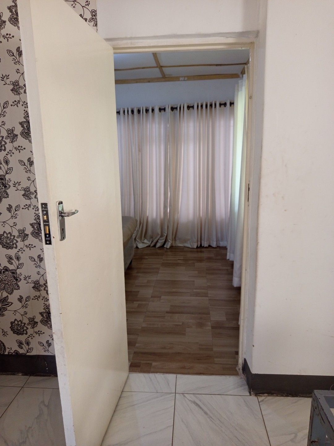 A room with a wooden floor, a bed, and a curtain-covered window.