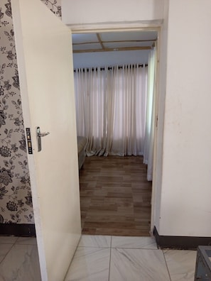 A room with a wooden floor, a bed, and a curtain-covered window.