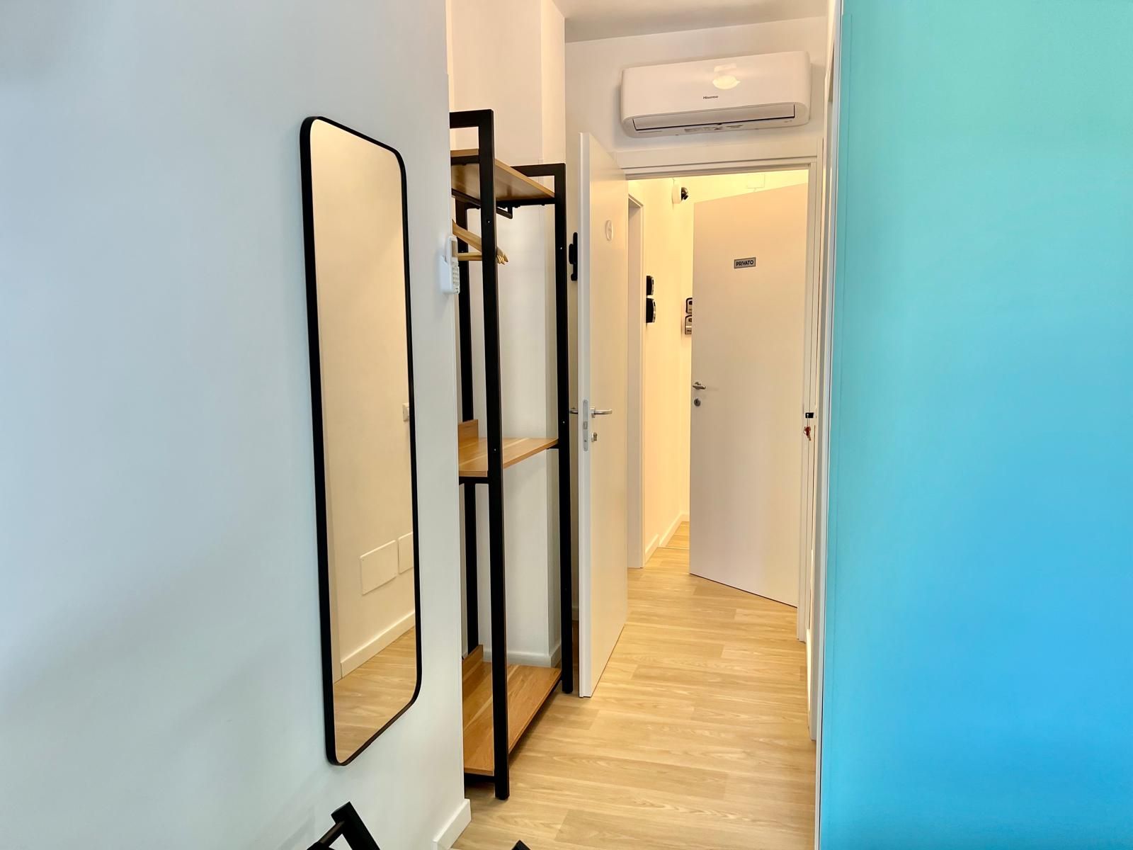 A hallway with a mirrored wardrobe, a wooden floor, and an air conditioning unit.