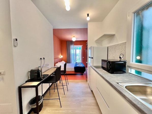 A compact hotel room with a kitchenette, a bed, a desk, and a view of the outdoors. - Luciano Queen's Guest House (Rome)