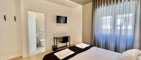 A hotel room with a bed, a desk, a television, and a bathroom visible through an open door.