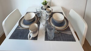 Mesa de jantar posta com pratos, tigelas, copos e talheres, com uma televisão de tela plana montada acima.