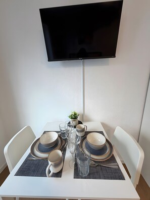 Ein Esszimmer mit gedecktem Tisch, Geschirr, Gläsern und Besteck, sowie einem flachbildfernseher an der Wand.