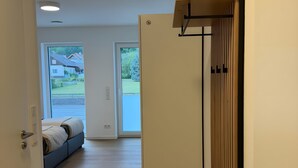 A hallway with a wooden floor, a bed with a view to the outside, and a door with a vertical blinds panel.