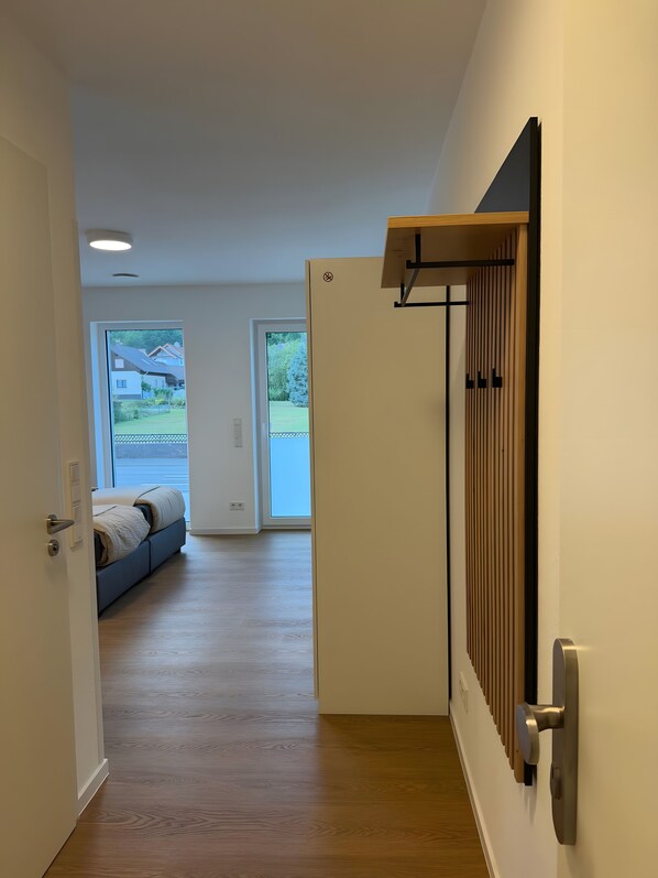Un pasillo con piso de madera, una cama con vistas al exterior y una puerta con paneles de persianas verticales.