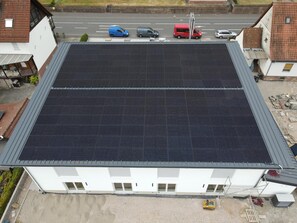 Un edificio con techo plano cubierto de paneles solares, un camino de entrada pavimentado y una calle con automóviles estacionados.