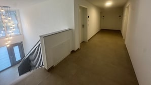 A hallway with a carpeted floor, white walls, and a staircase with a metal railing.