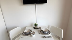 A dining area with a white table, two chairs, a flat-screen TV mounted on the wall, and a small plant on the table. - Apartment in A Hotel 'Werner Apartments Mecklar 11' with Shared Terrace, Shared Garden and Wi-Fi (Ludwigsau)