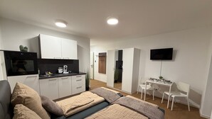 A modern apartment with a kitchenette, a bed with beige bedding, a desk with a chair, and a flat-screen TV mounted on the wall. - Apartment in A Hotel 'Werner Apartments Mecklar 11' with Shared Terrace, Shared Garden and Wi-Fi (Ludwigsau)