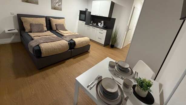 A modern bedroom with a bed, a small kitchenette, and a dining area with tableware. - Apartment in A Hotel 'Werner Apartments Mecklar 11' with Shared Terrace, Shared Garden and Wi-Fi (Ludwigsau)