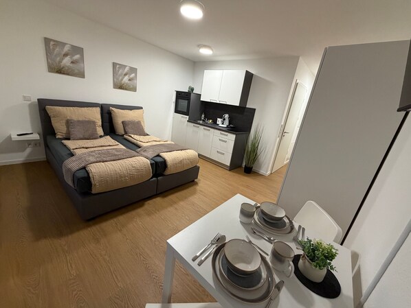 Ein modernes Schlafzimmer mit einem Bett, einer kleinen Küchenzeile und einem Essbereich mit Geschirr.